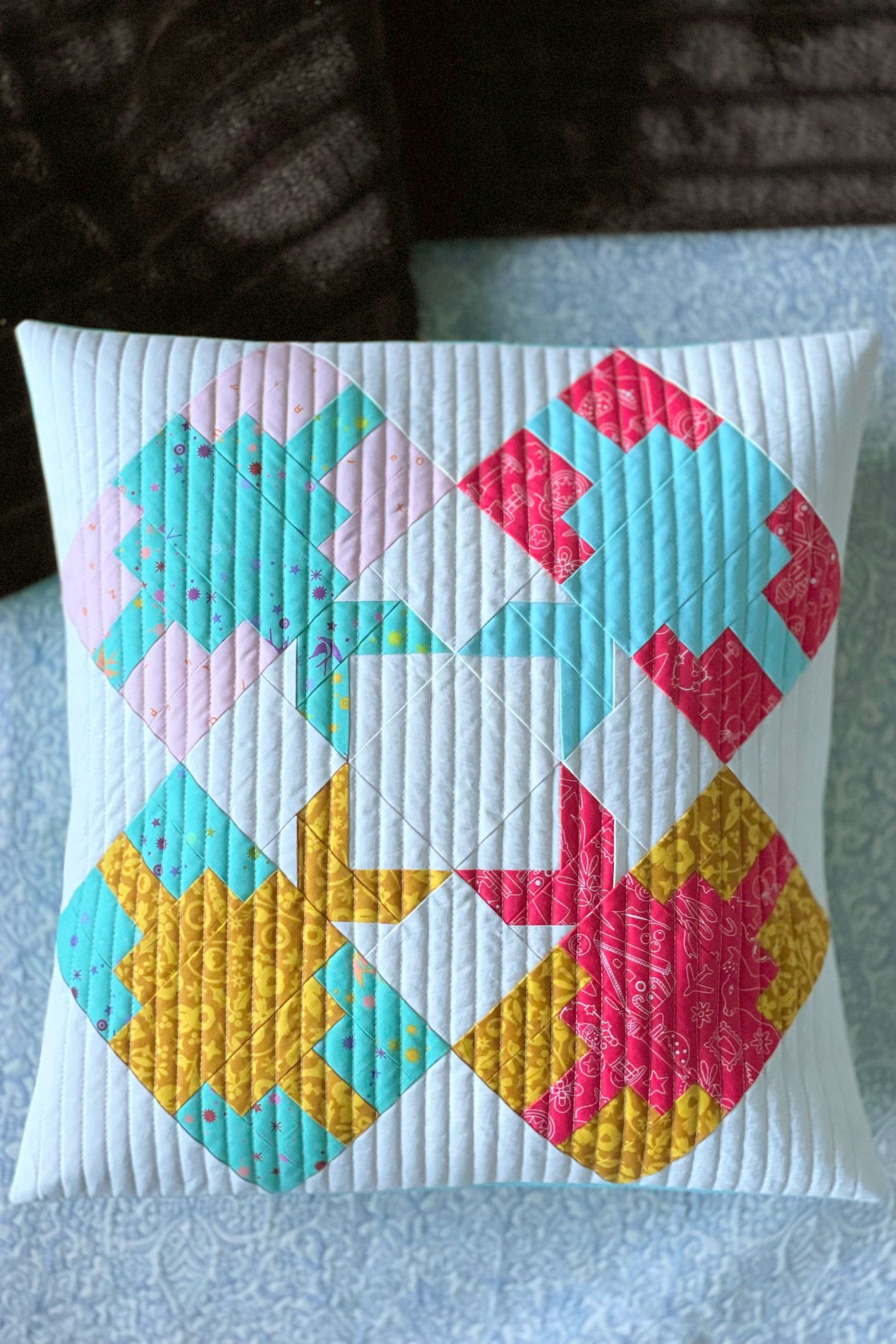 blue, pink and yellow pieced pillow, quilted on bed
