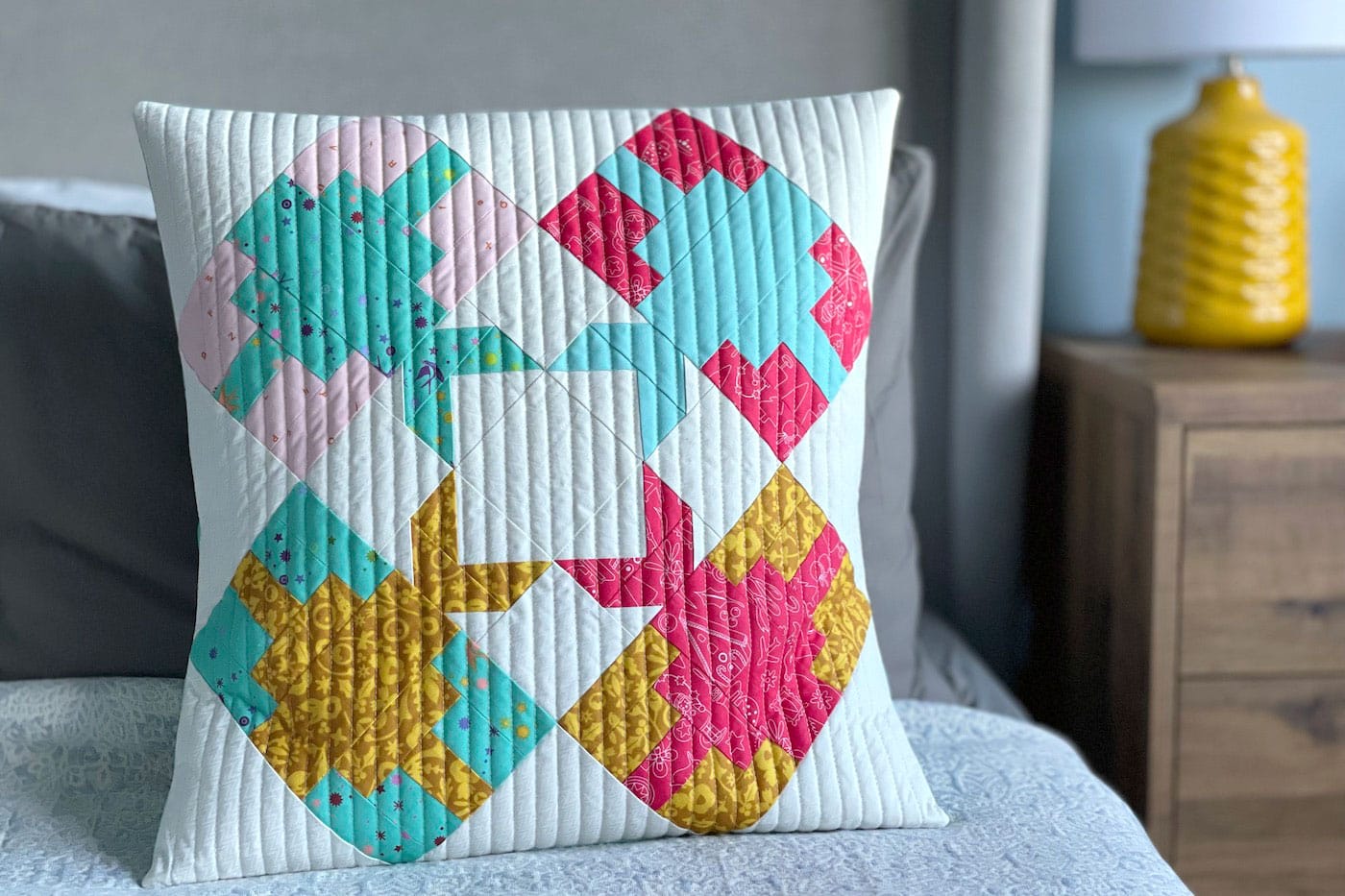 blue, pink and yellow pieced pillow, quilted on bed