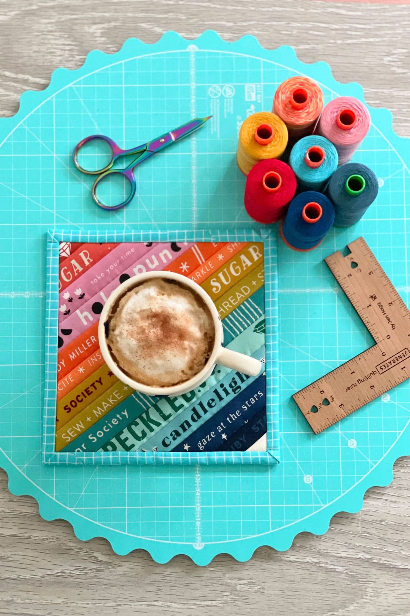 colorful mug rug on wood table with mug cutting mat and thread