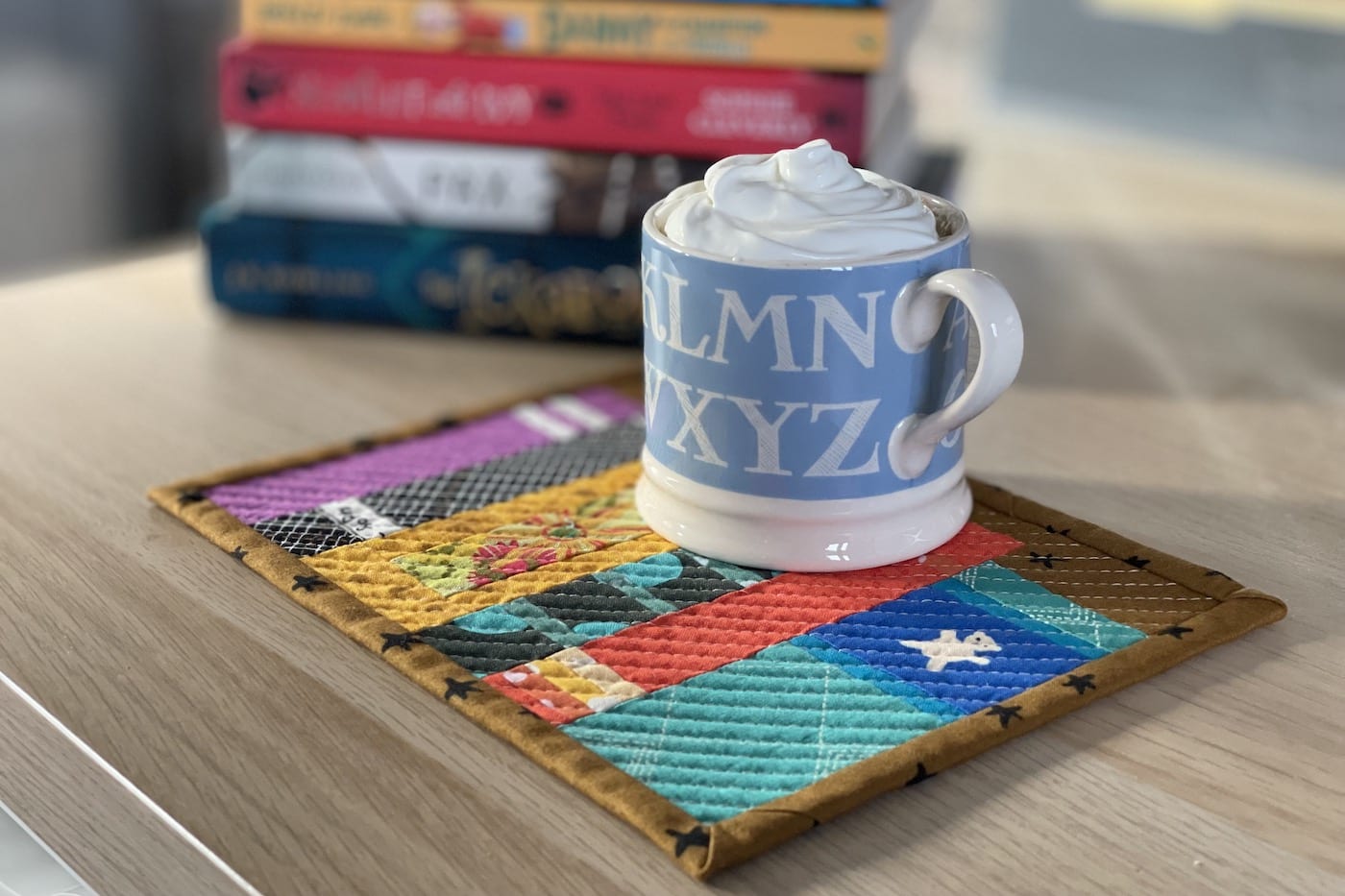 Mug rug and mug with ship cream and cocoa with books on wood table