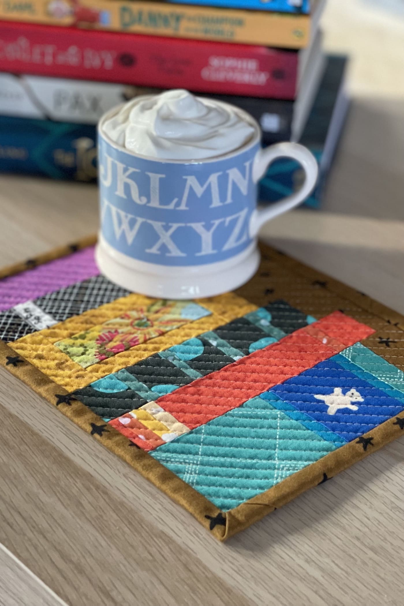 Mug rug and mug with ship cream and cocoa with books on wood table