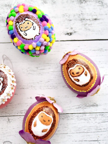 multiple blown egg ornaments with painted hedgehogs on white wood table