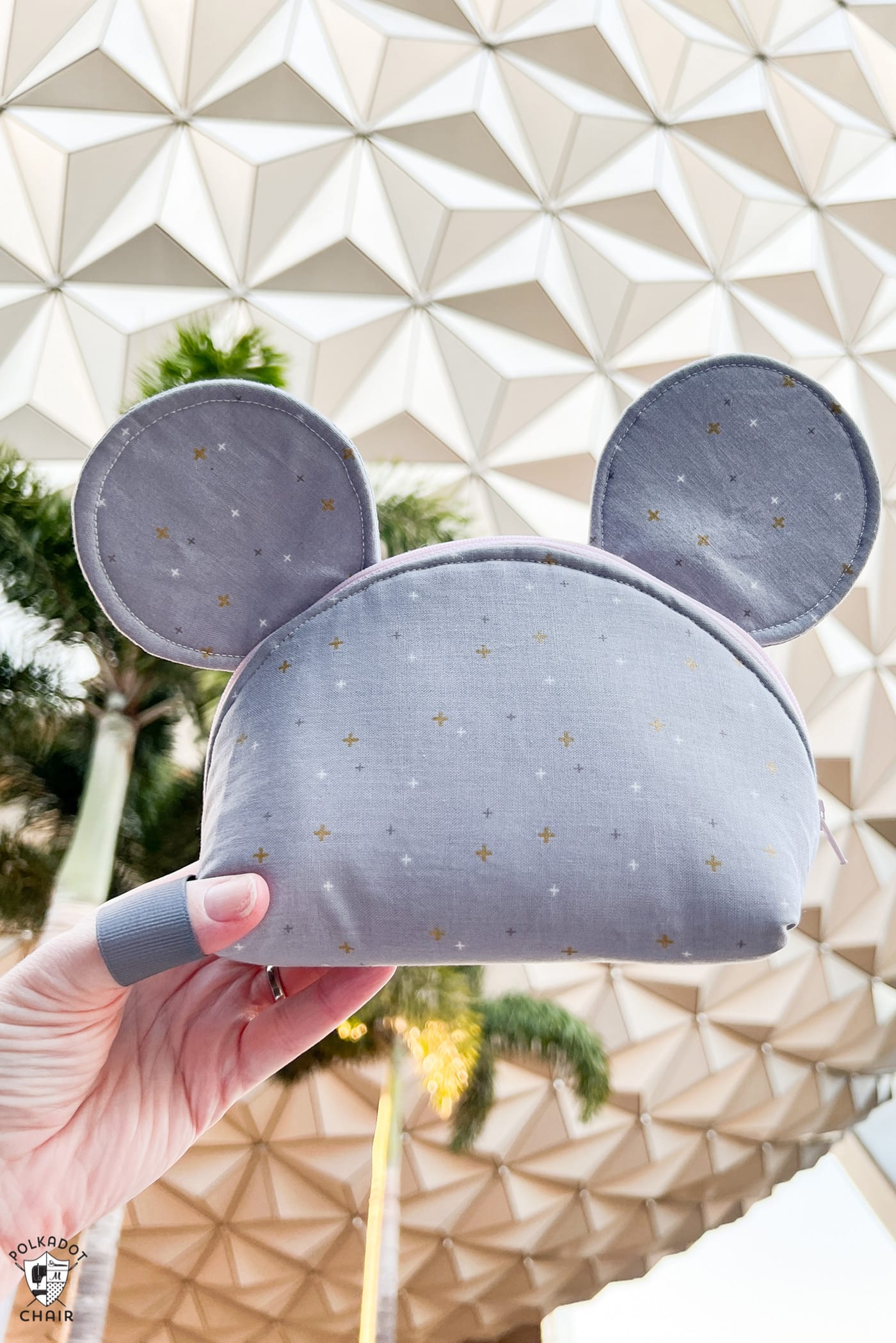 woman holding gray mouse zip pouch in front of epcot ball