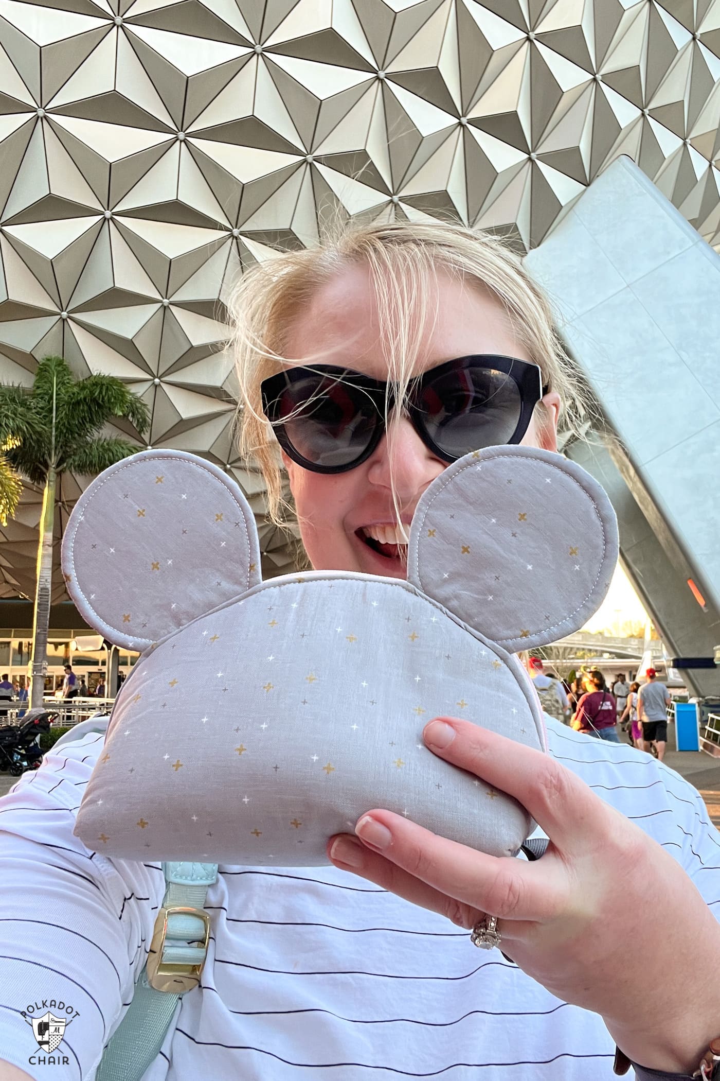 woman holding gray mouse zip pouch in front of epcot ball