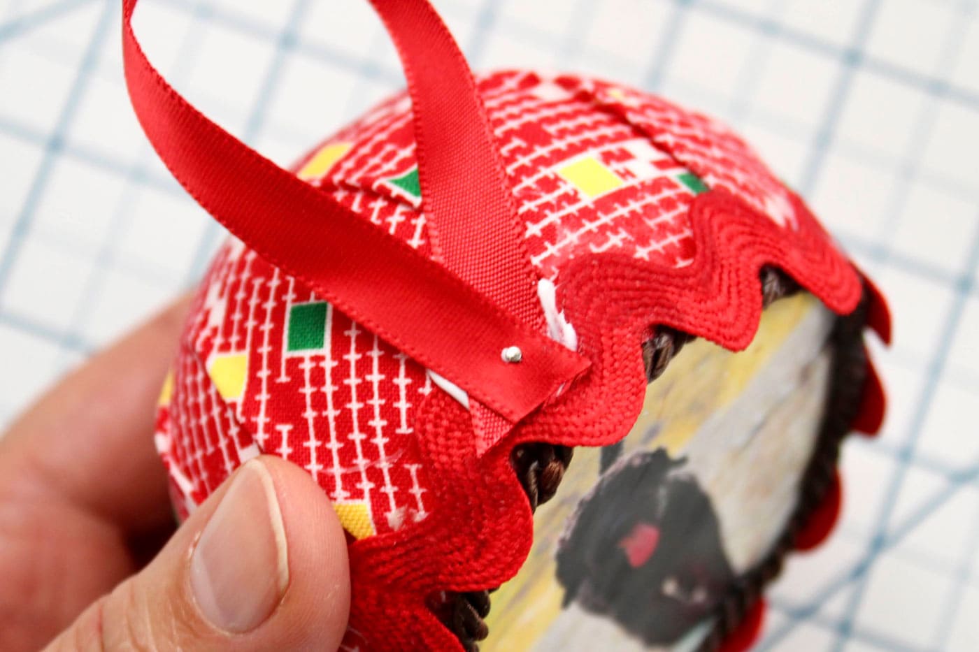 close up of round fabric ornament with trim and ribbon attached