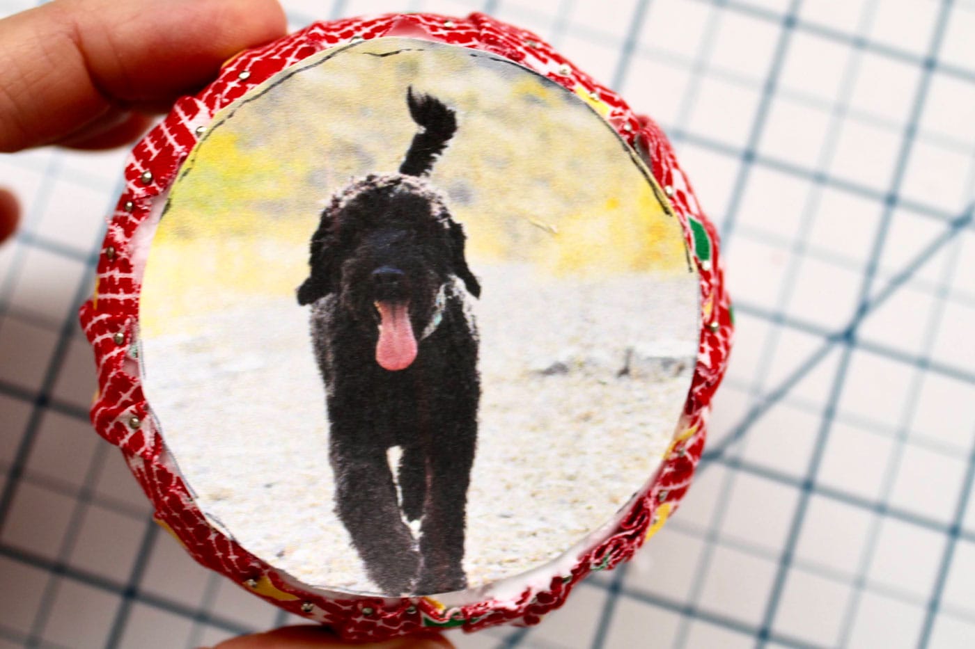 close up of round fabric ornament with trim and ribbon attached and a photo