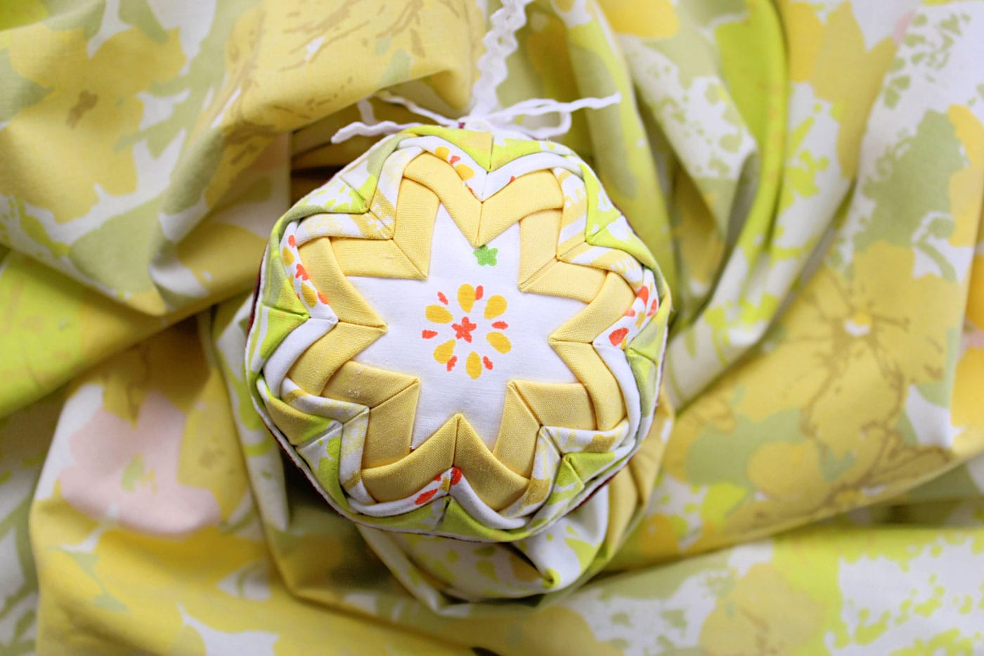 yellow and white vintage folded fabric ornament on white table with fabric scraps