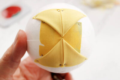 yellow fabric with folds, pin and white styrofoam ball