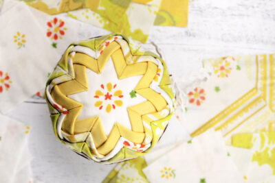 yellow and white vintage folded fabric ornament on white table with fabric scraps