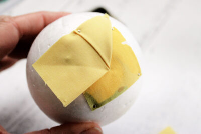 yellow fabric with folds, pin and white styrofoam ball