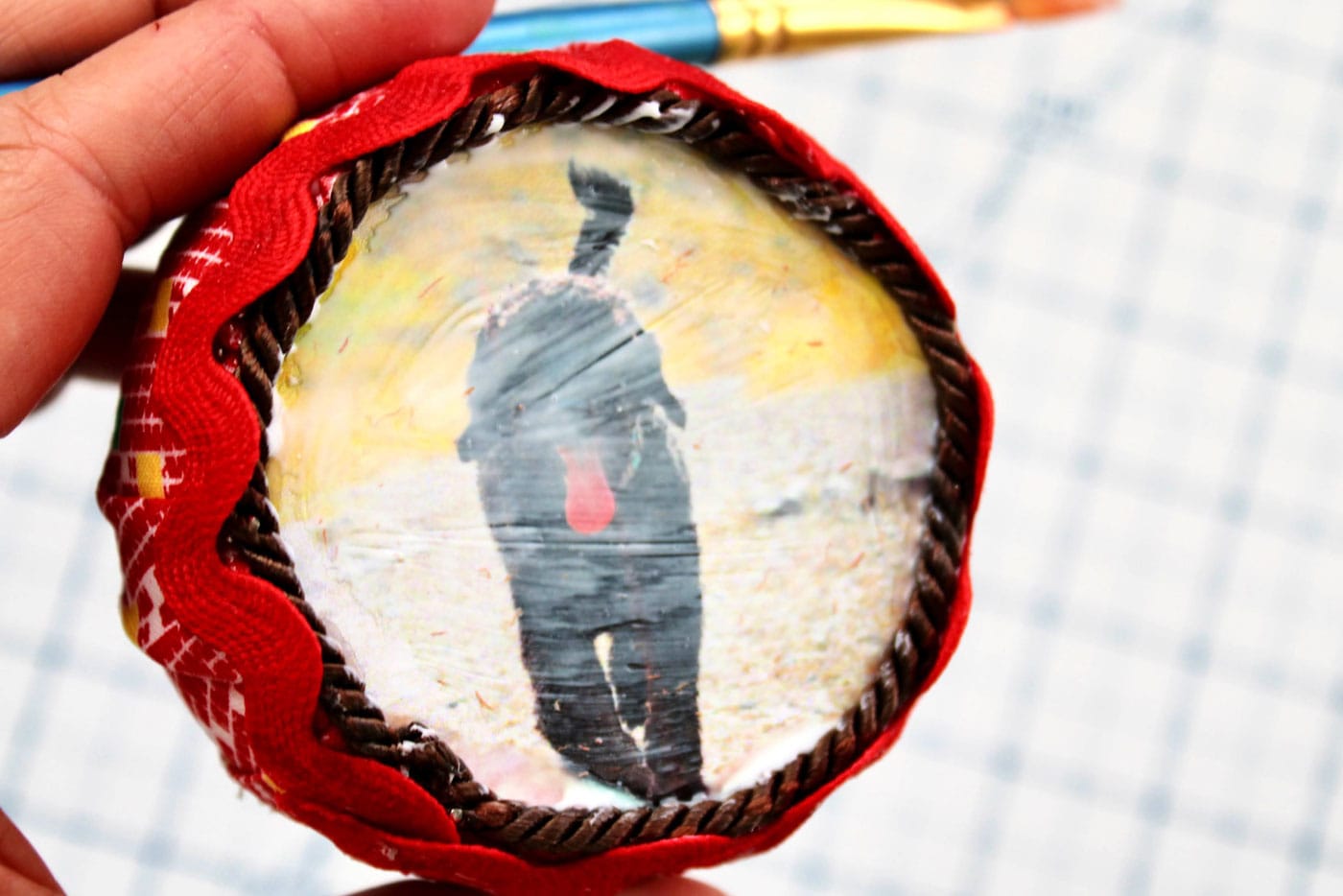 close up of round fabric ornament with trim and ribbon attached and a photo