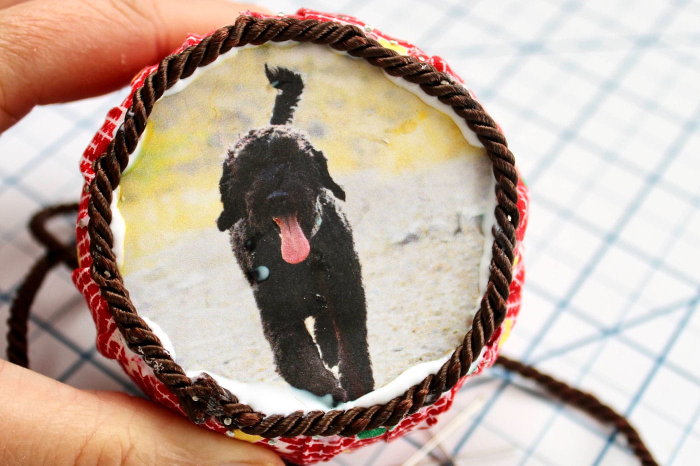 close up of round fabric ornament with trim and ribbon attached and a photo