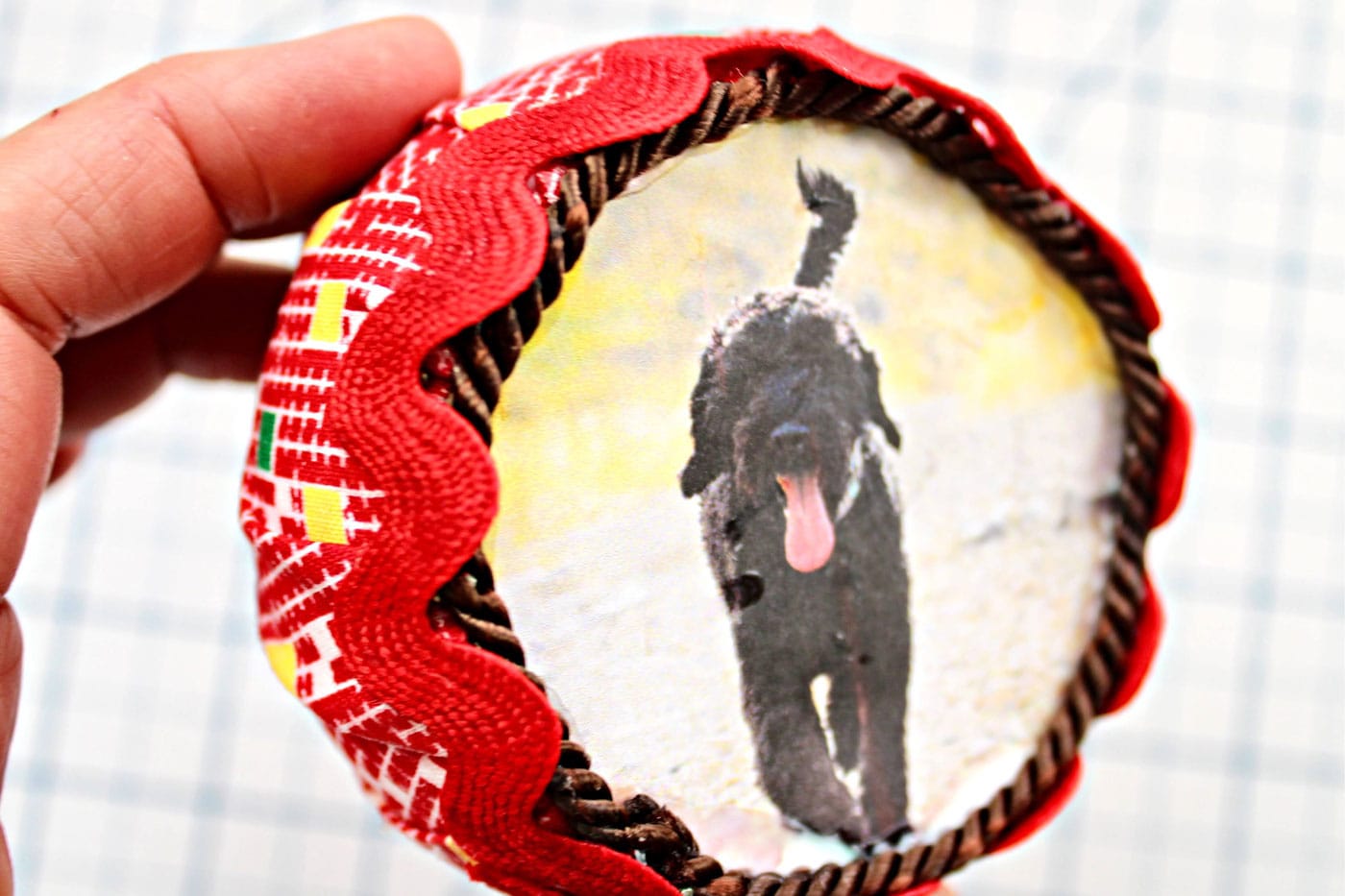 close up of round fabric ornament with trim and ribbon attached and a photo