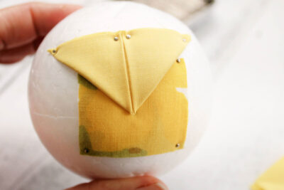 yellow fabric with folds, pin and white styrofoam ball