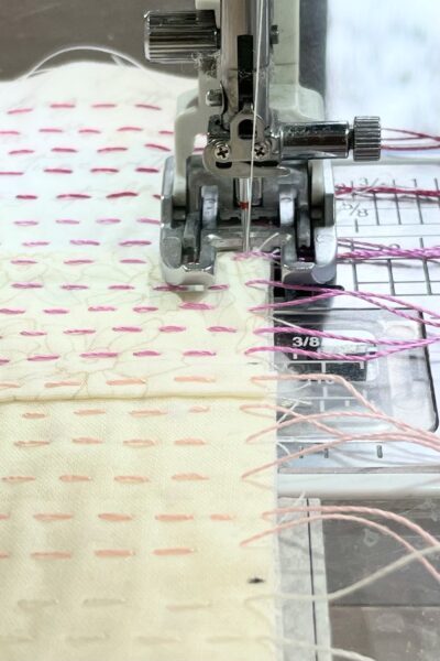 close up of cream fabrics stitched together on sewing machine with pink hand stitching and needle