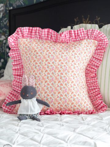 Pink and yellow ruffled pillow with stuffed animal on white bedding