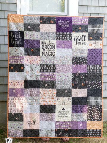 Purple ivory and gray Halloween quilt in front of gray house