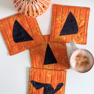 four orange and black pumpkin face coasters on table with coffee mug