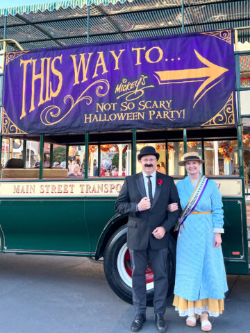 couple in costumes in front of sign at disneyworld