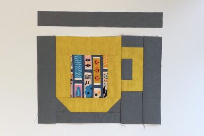 yellow cup quilt block with gray fabric on table