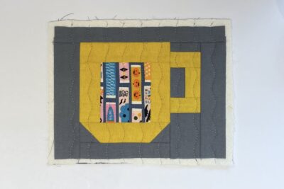 yellow cup quilt block with gray fabric on table