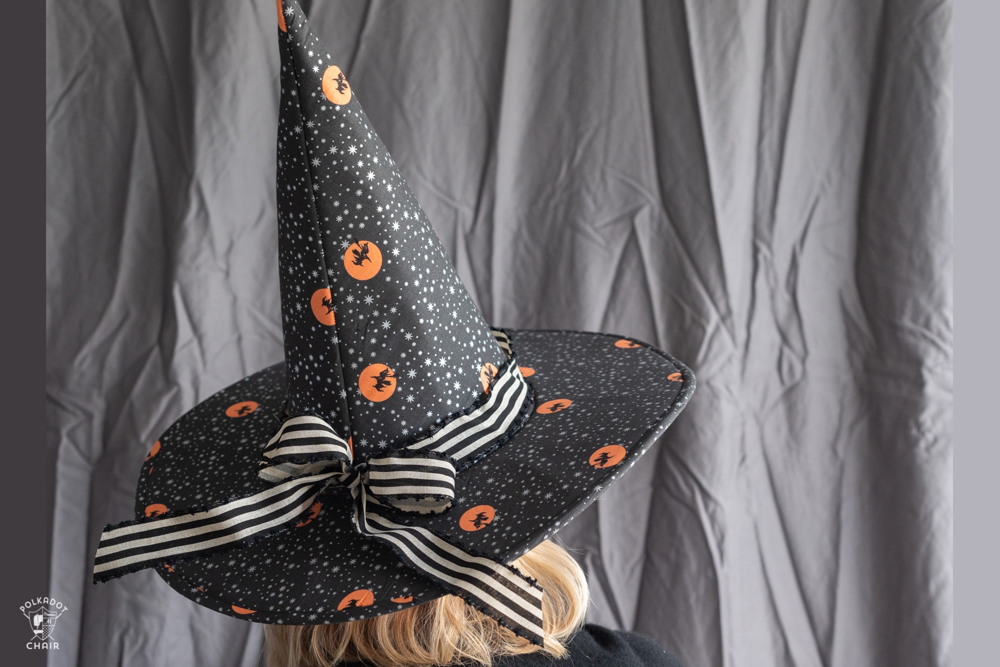 woman wearing patchwork witch hat in front of gray wall