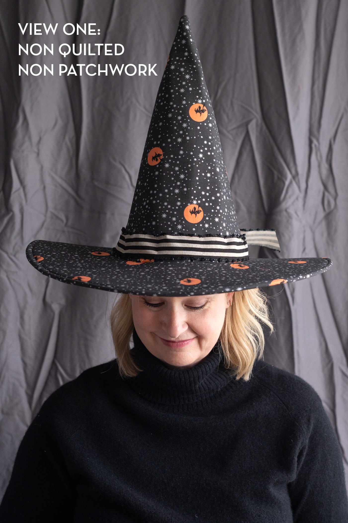 woman wearing patchwork witch hat in front of gray wall