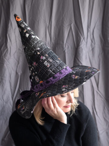 woman wearing patchwork witch hat in front of gray wall