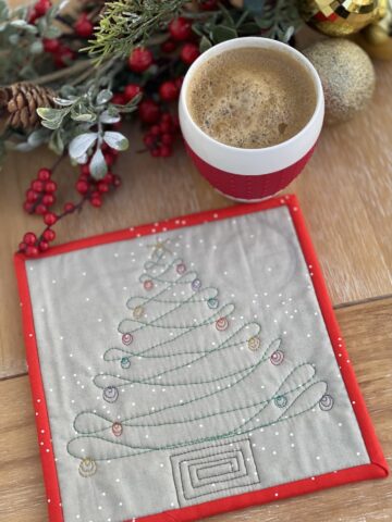 gray and red mug rug on wood table with coffee cup and christmas decorations