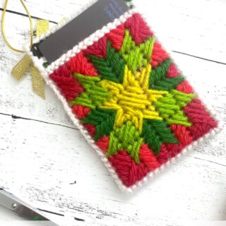 red, green and yellow plastic canvas gift card holder on white wood table