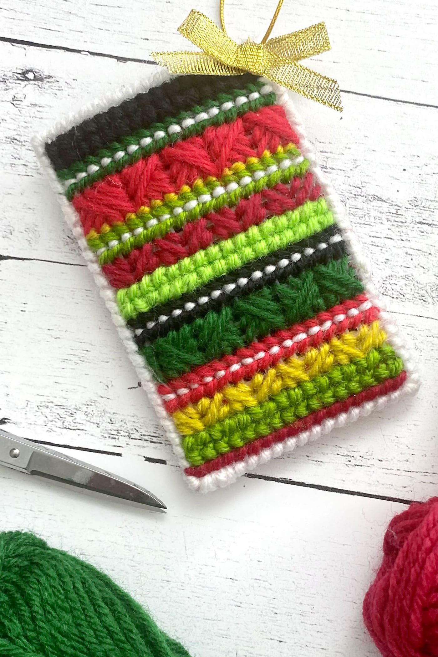 red, green and yellow plastic canvas gift card holder on white wood table