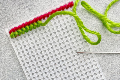 plastic canvas construction steps in detail with yarn, needles on white table