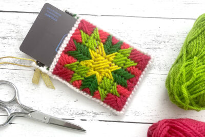 red, green and yellow plastic canvas gift card holder on white wood table