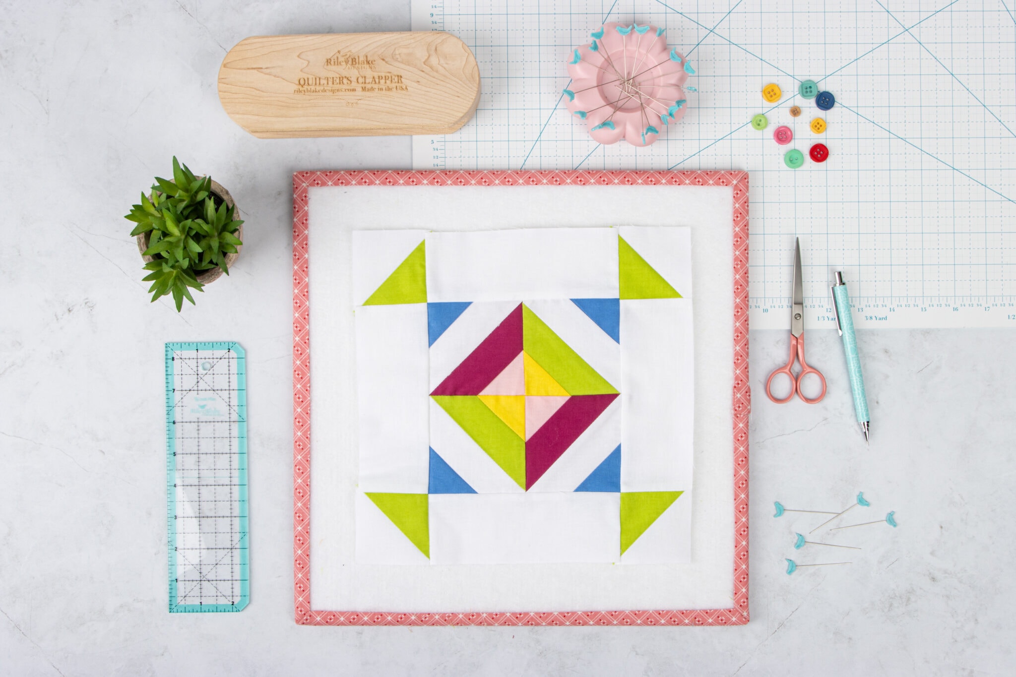 blue red and green quilt block on white table with sewing notions