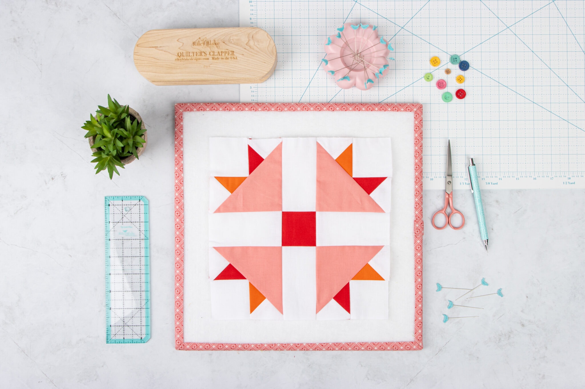 pink and coral quilt block on white wood table with sewing notions