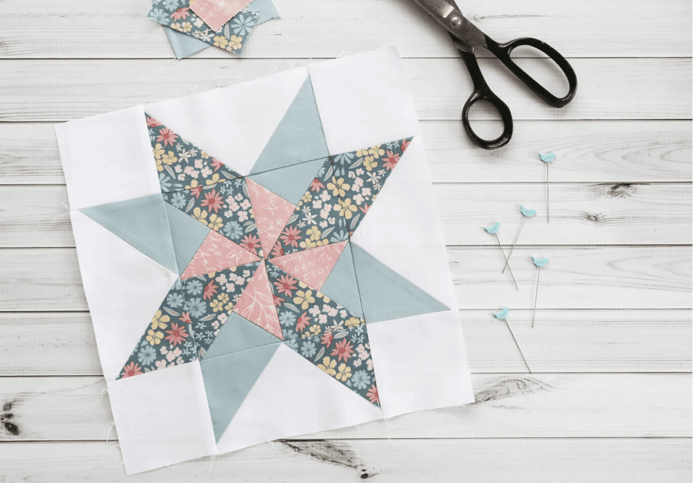 blue and pale pink quilt block on  wood table with sewing notions