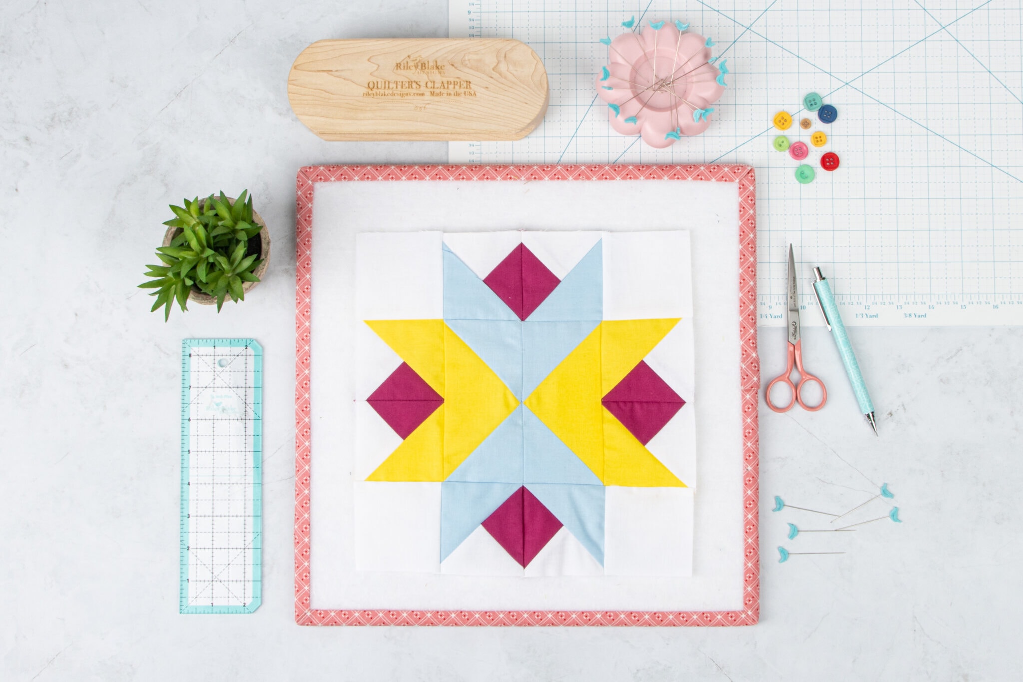 Yellow, blue and red quilt block on white table with quilting notions