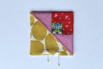 squares of pink, red and green fabric on white table with pins - construction steps of fabric bookmark