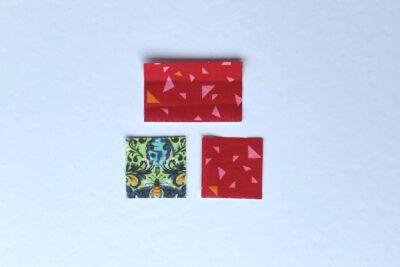 squares of pink, red and green fabric on white table with pins - construction steps of fabric bookmark