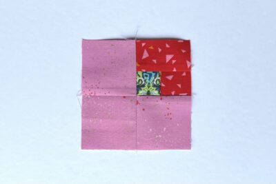 squares of pink, red and green fabric on white table with pins - construction steps of fabric bookmark