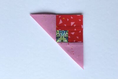 squares of pink, red and green fabric on white table with pins - construction steps of fabric bookmark