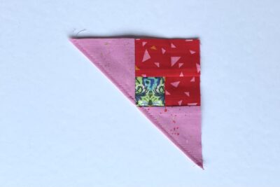 squares of pink, red and green fabric on white table with pins - construction steps of fabric bookmark