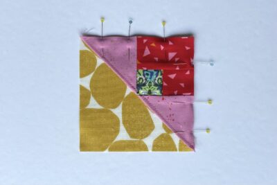 squares of pink, red and green fabric on white table with pins - construction steps of fabric bookmark