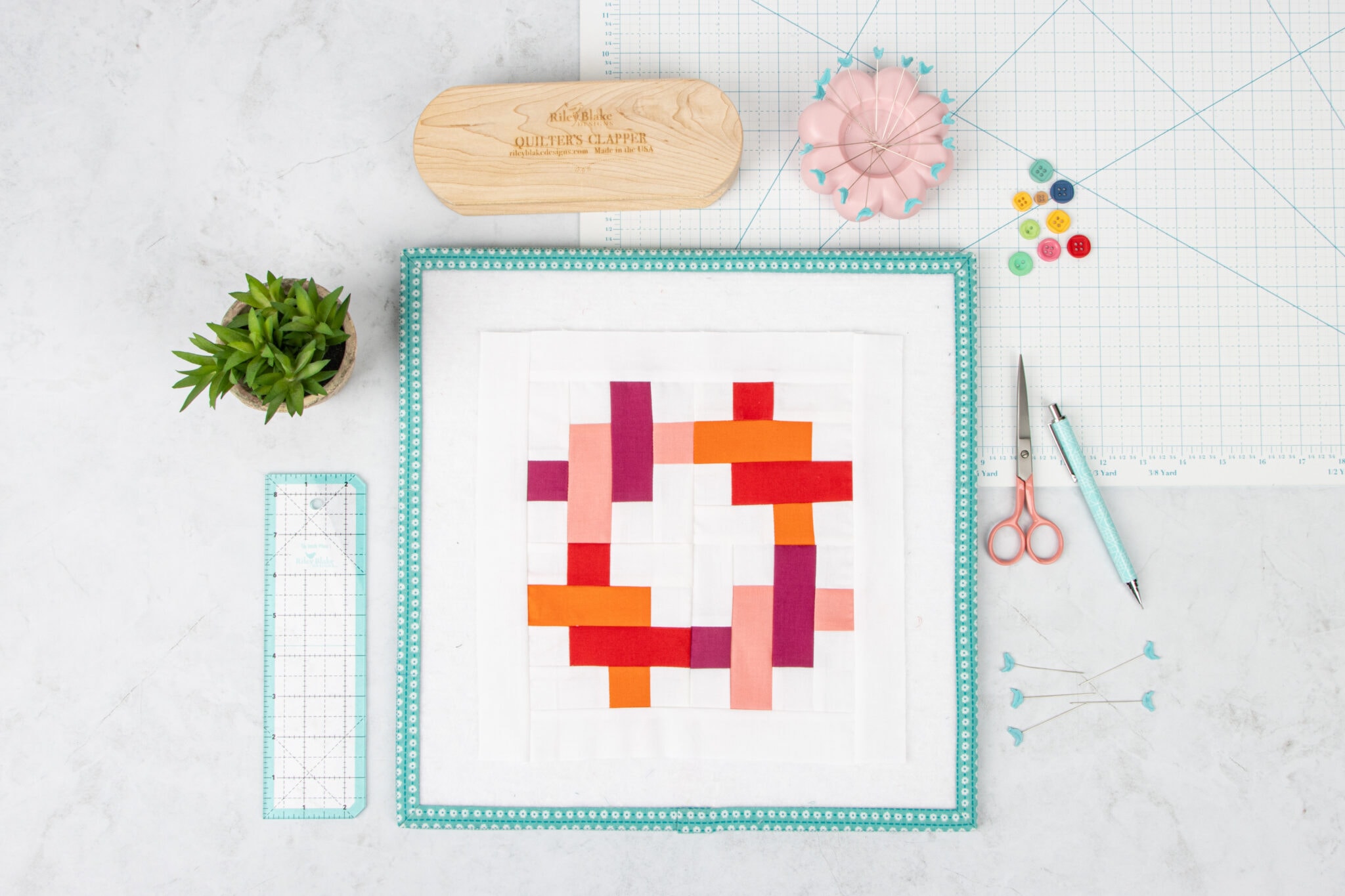 pink, red and orange quilt block on white table with sewing notions