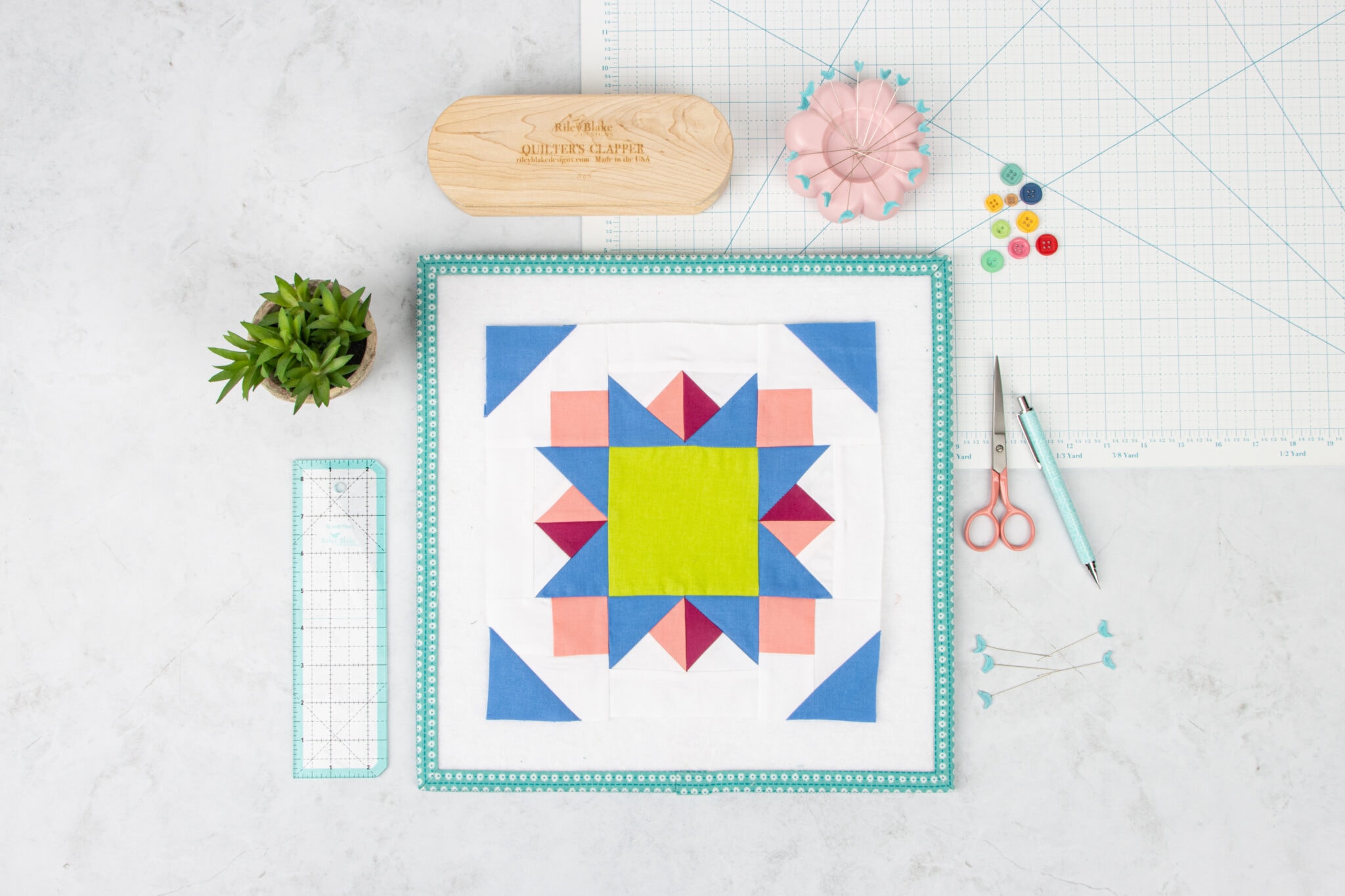 Blue, green and pink geometric quilt block on white table with sewing notions