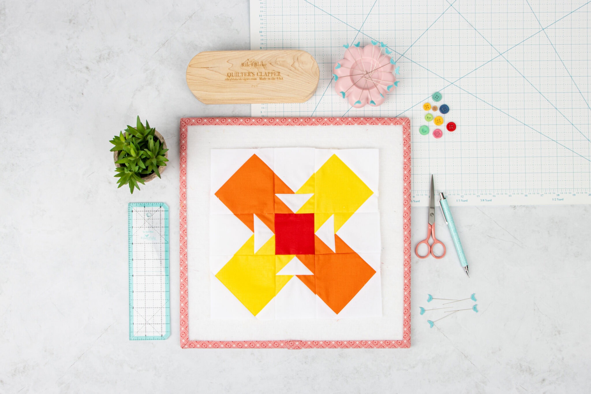 orange and yellow quilt block on white table with sewing notions