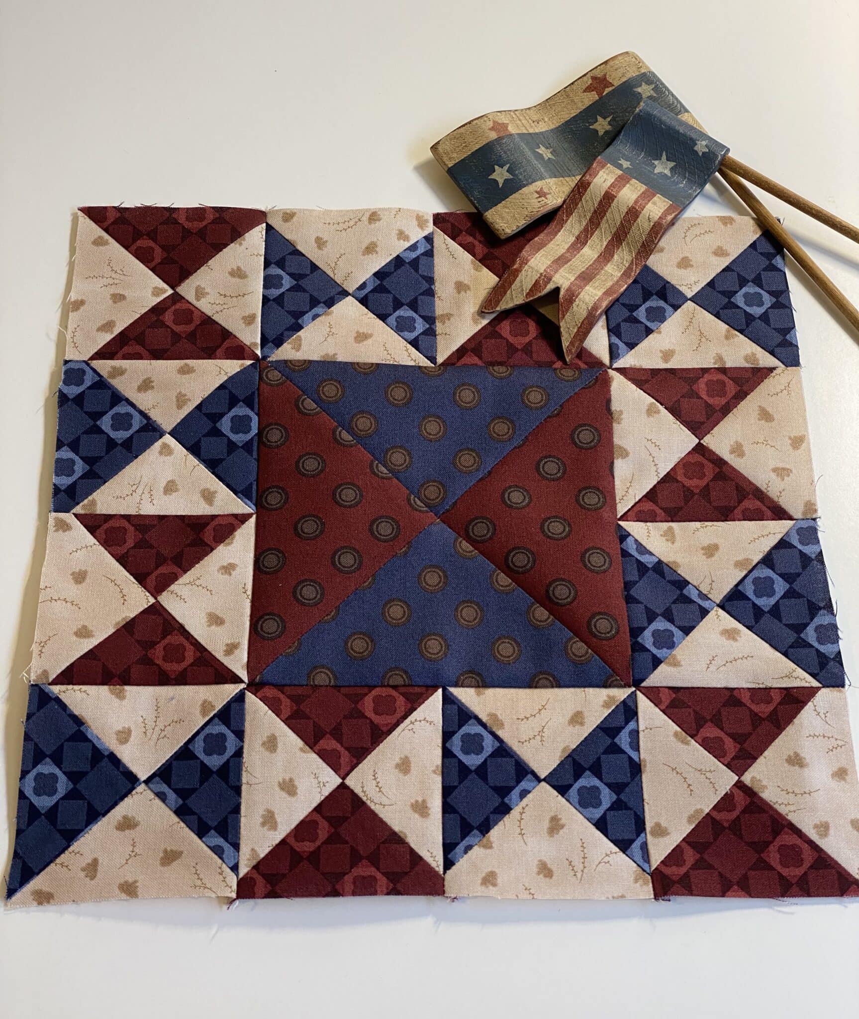 Red, beige and blue quilt block on white table with antique flag