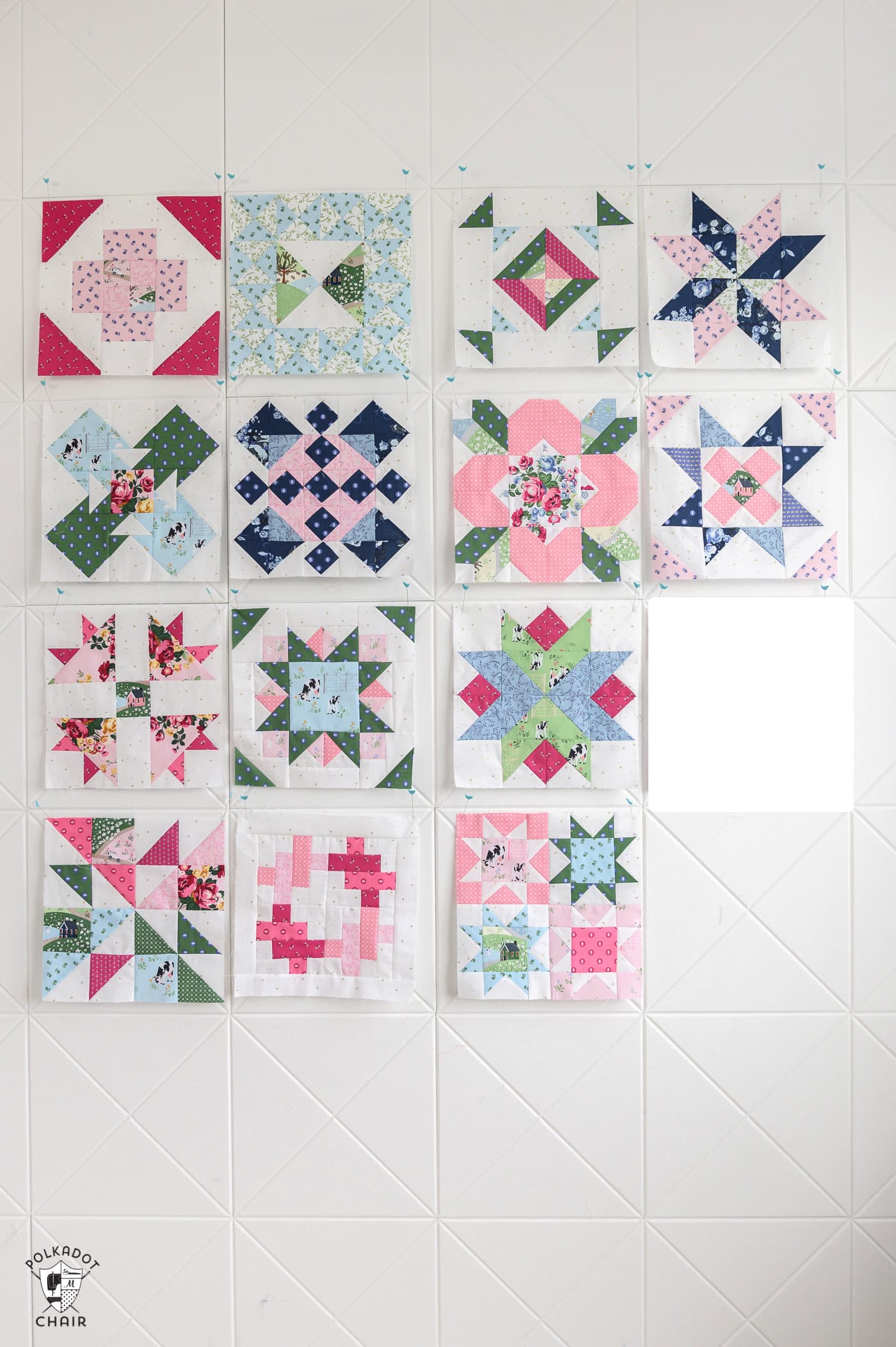 fourteen quilt blocks pinned to a white pinboard wall