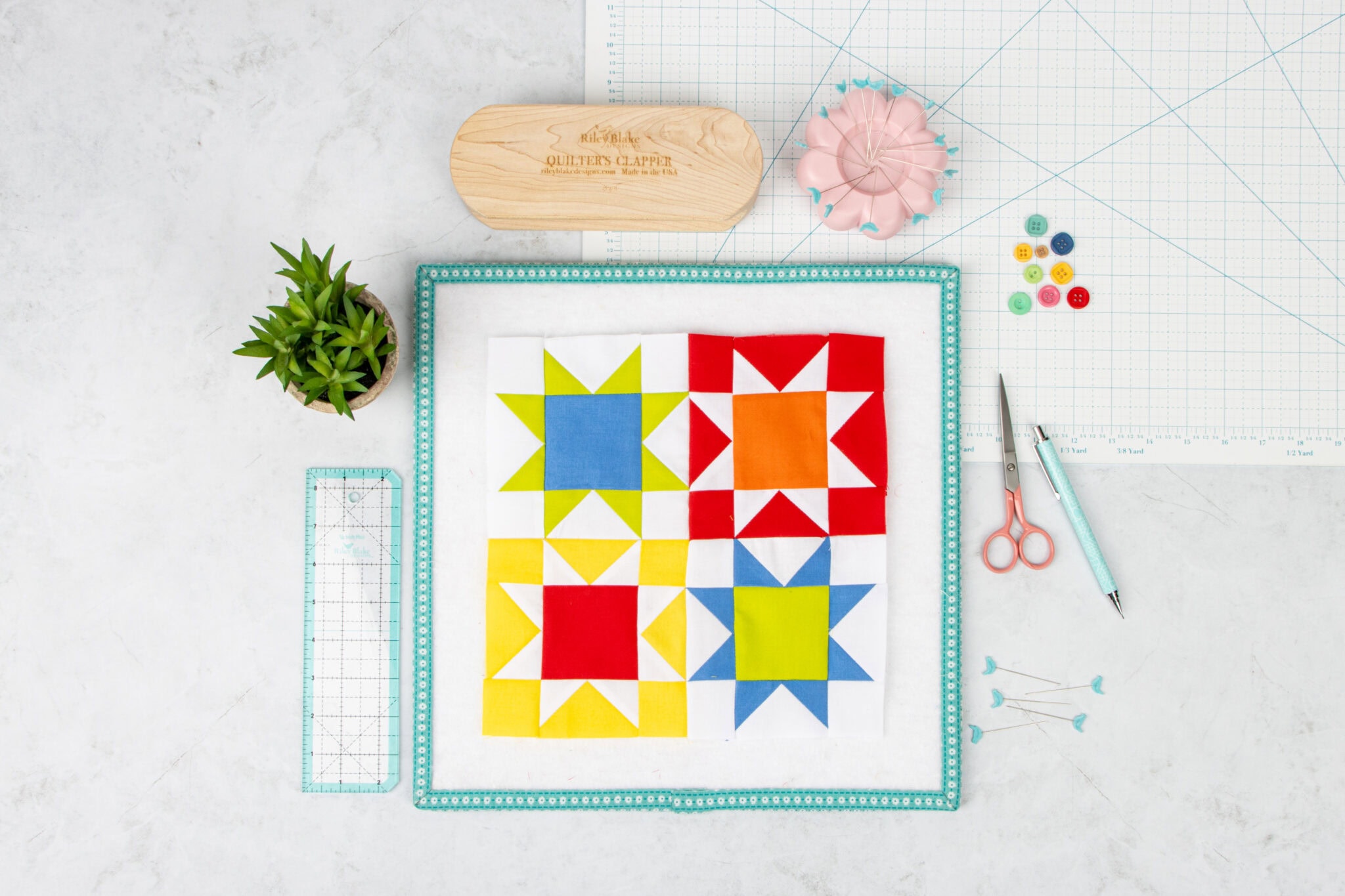 red, blue and green quilt block on white wood table with colorful sewing notions