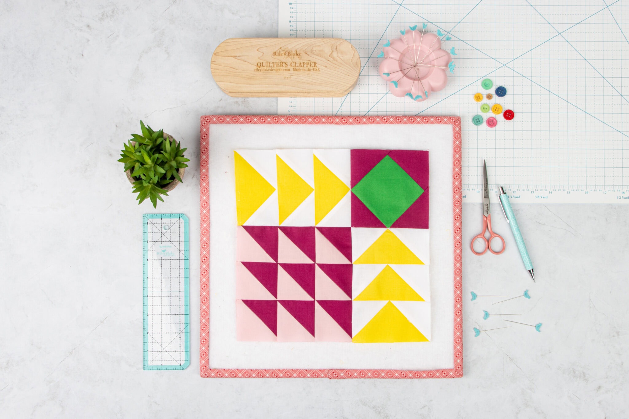 Purple, yellow and teal quilt block on white wood table with sewing notions